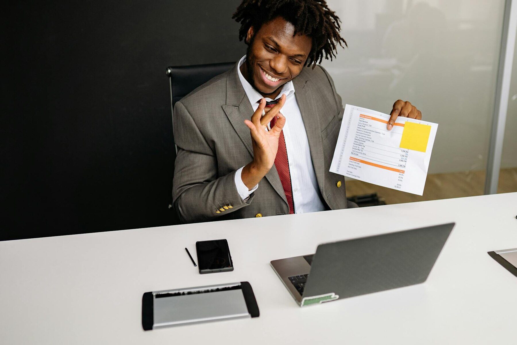 A man in a suit holding a piece of paper while looking at a laptop in front of him